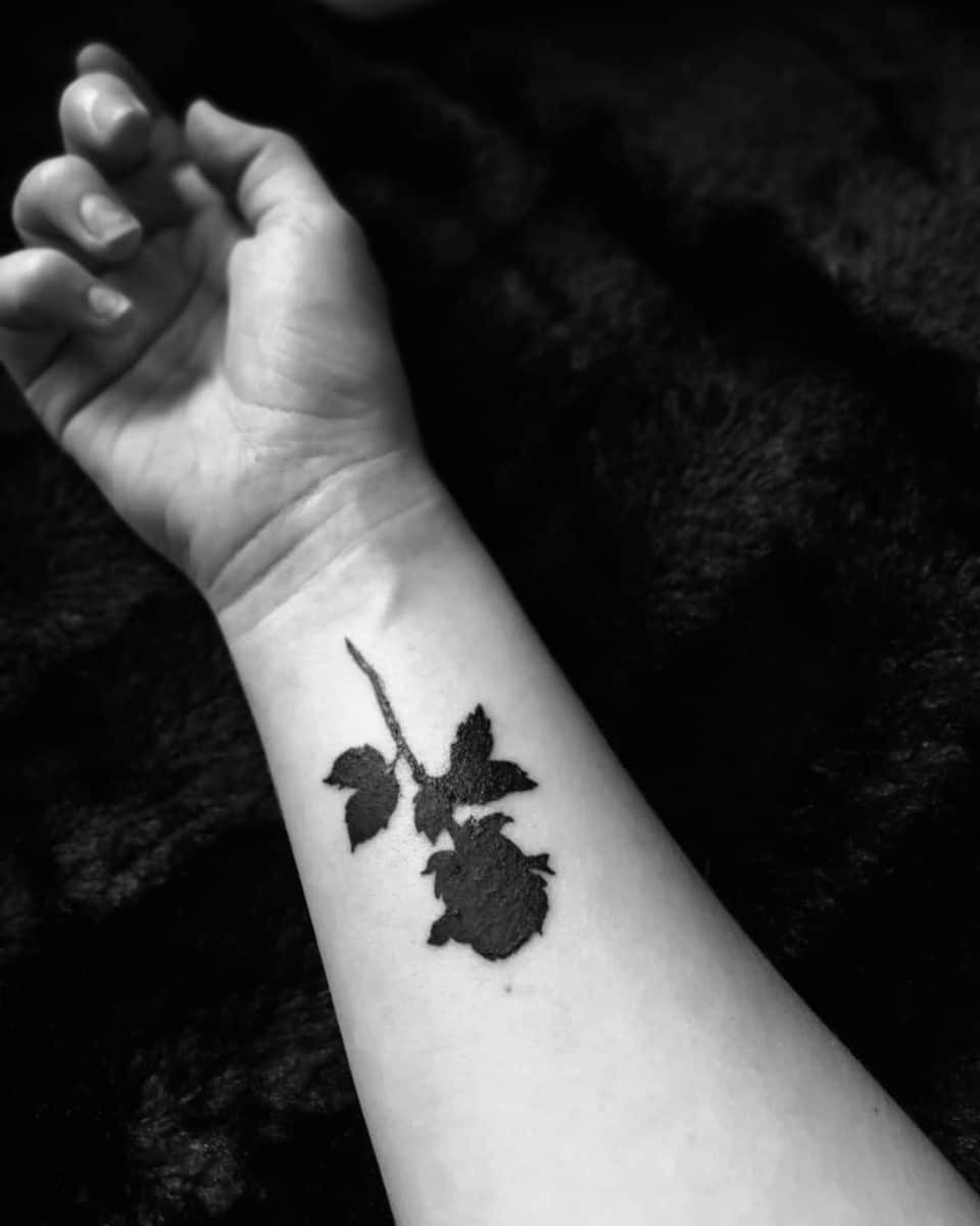 A black rose silhouette tattoo on a wrist