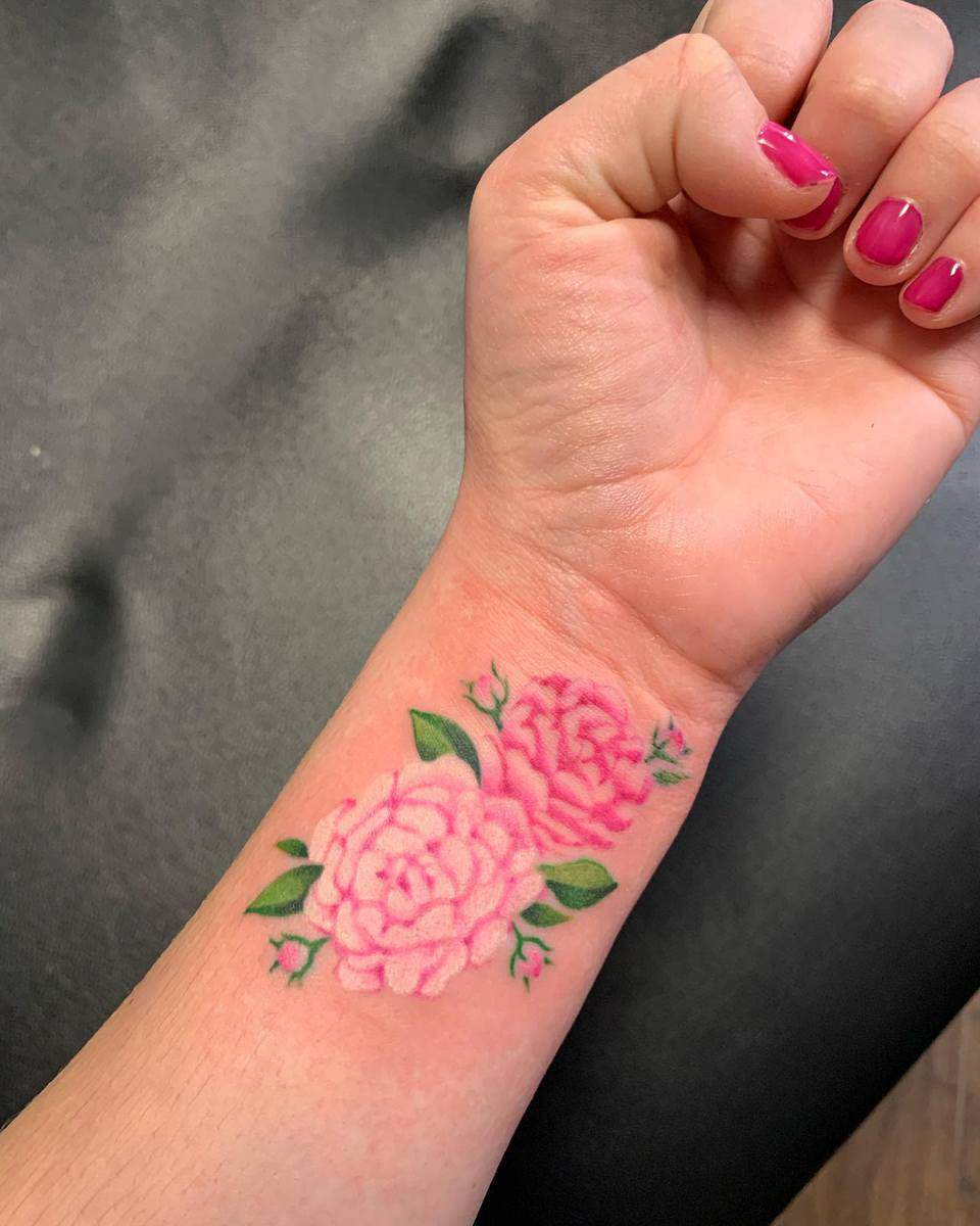 Foreground of a wrist with a tattoo of two pink flowers and green leaves