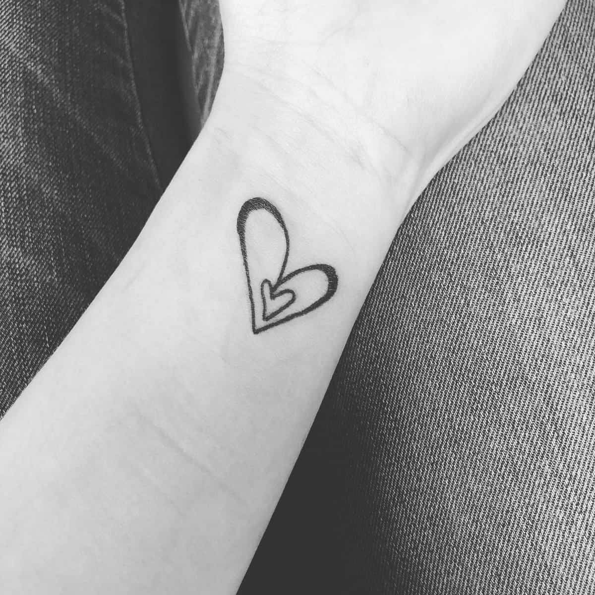 A small heart tattoo with an inner heart on a wrist, shown in black and white