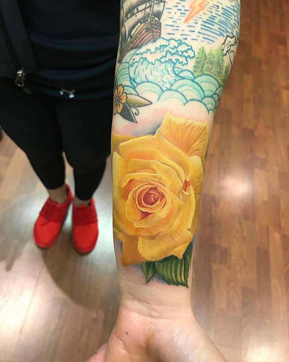 Wrist tattoo featuring a vibrant yellow rose with other floral and maritime designs
