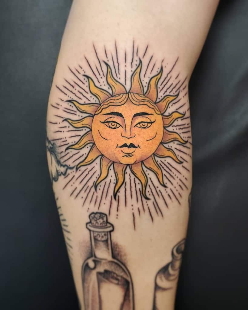 A tattoo of a sun with a face on an arm, surrounded by rays and bottles below it
