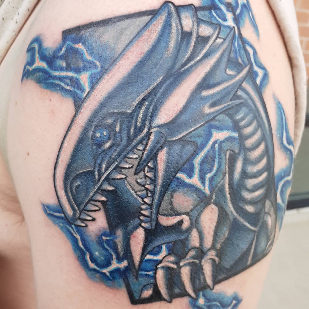 Tattoo of a fierce dragon-like creature with electric blue accents on an arm