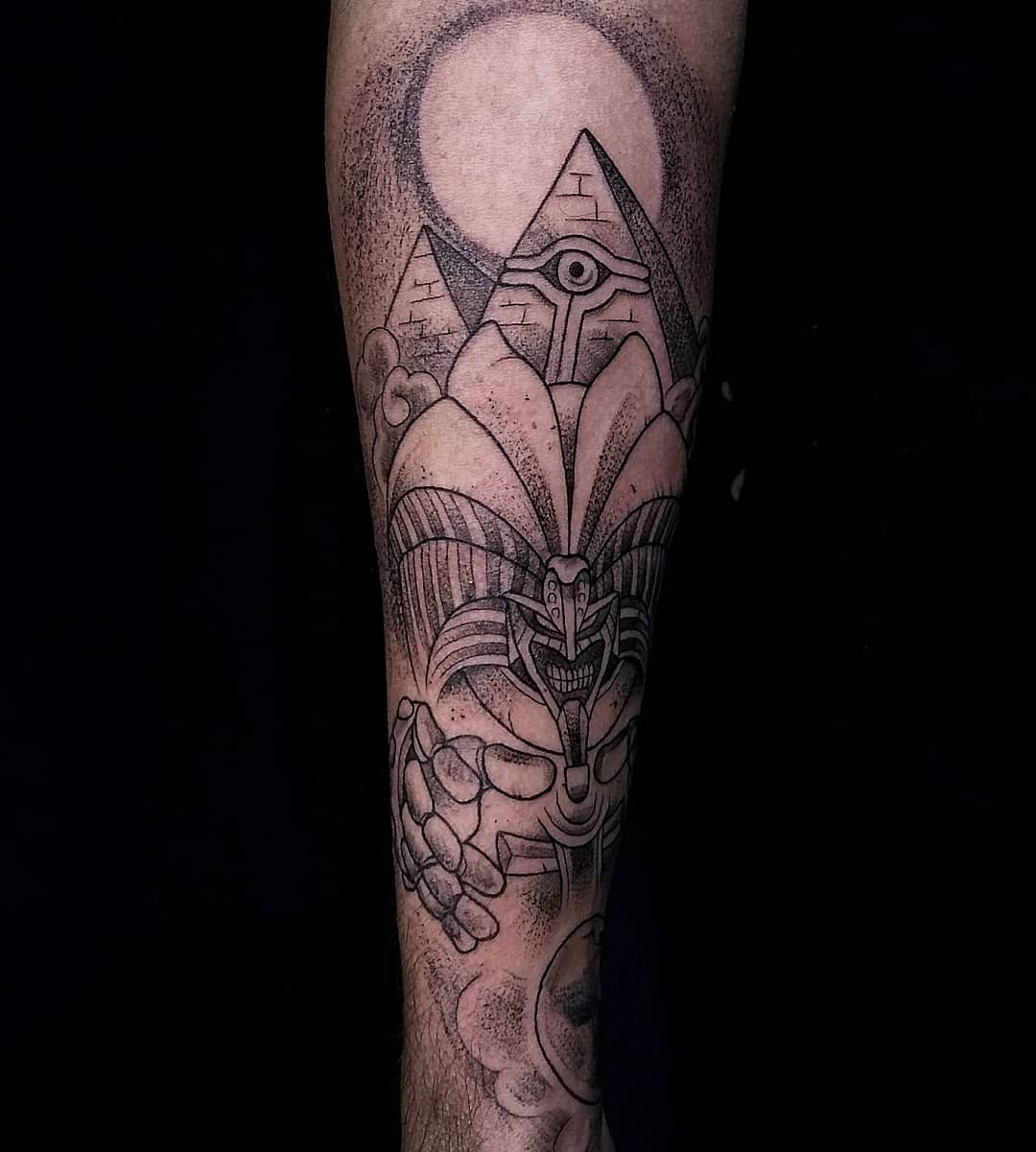 Forearm tattoo with pyramids, an eye, and a mythical creature design
