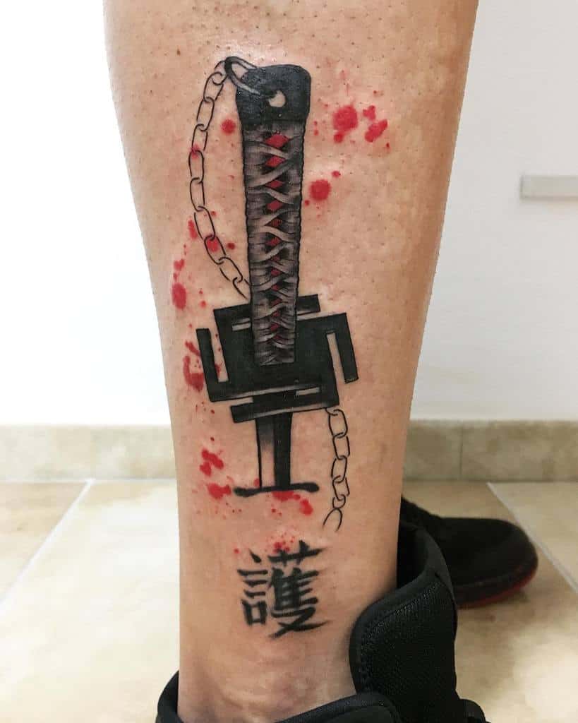 Colorful tattoo of Ichigo Kurosaki’s Zanpakutō from Bleach, featuring the handle with chain detail, abstract black shapes, red splatter effects, and kanji