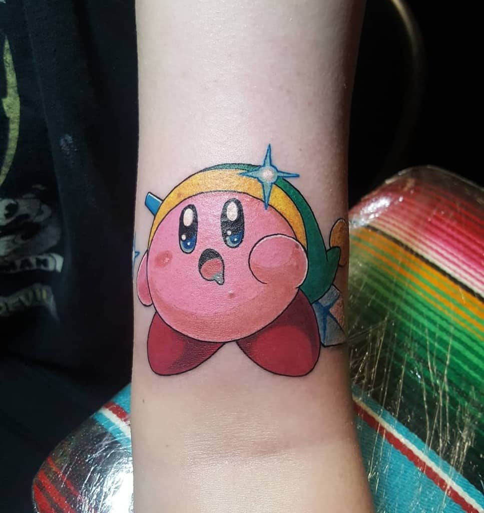 Colorful tattoo of Kirby dressed as Link from The Legend of Zelda, wearing a green hat with a shining blue gem