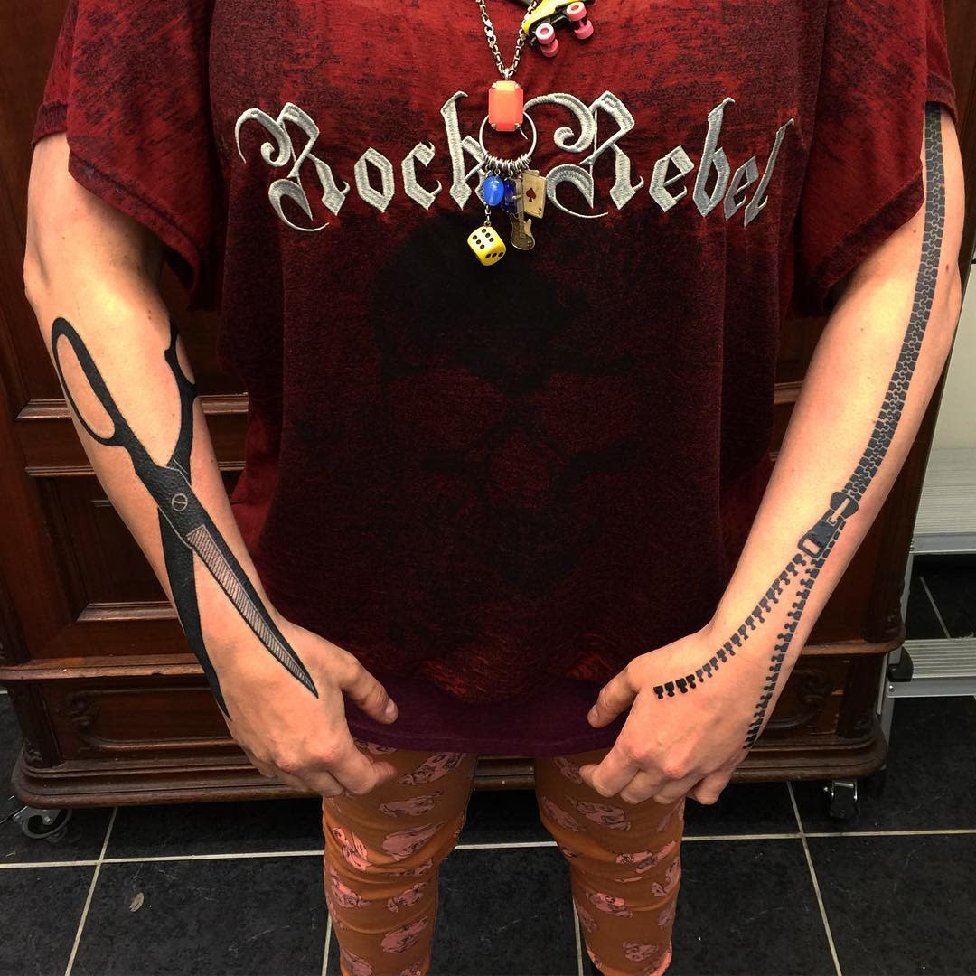 Individual with zipper and scissor tattoos on arms