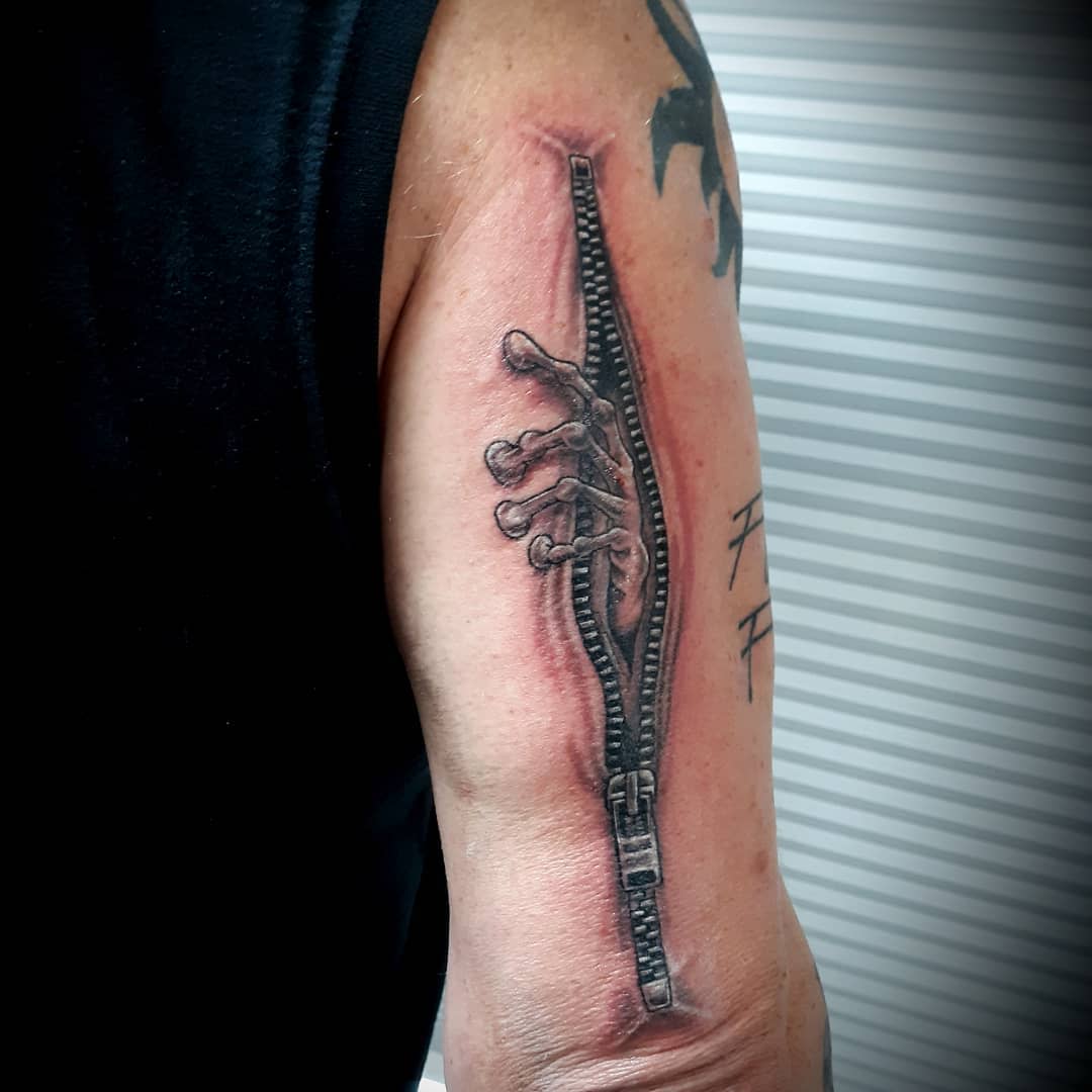 Tattoo of a hand emerging from an unzipped zipper on an arm
