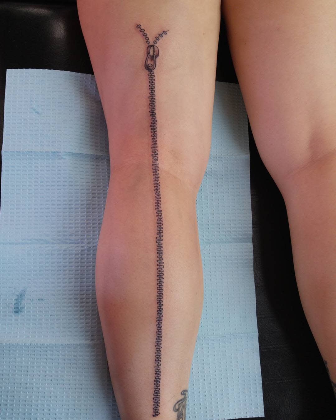 Tattoo of a long zipper on the back of a leg