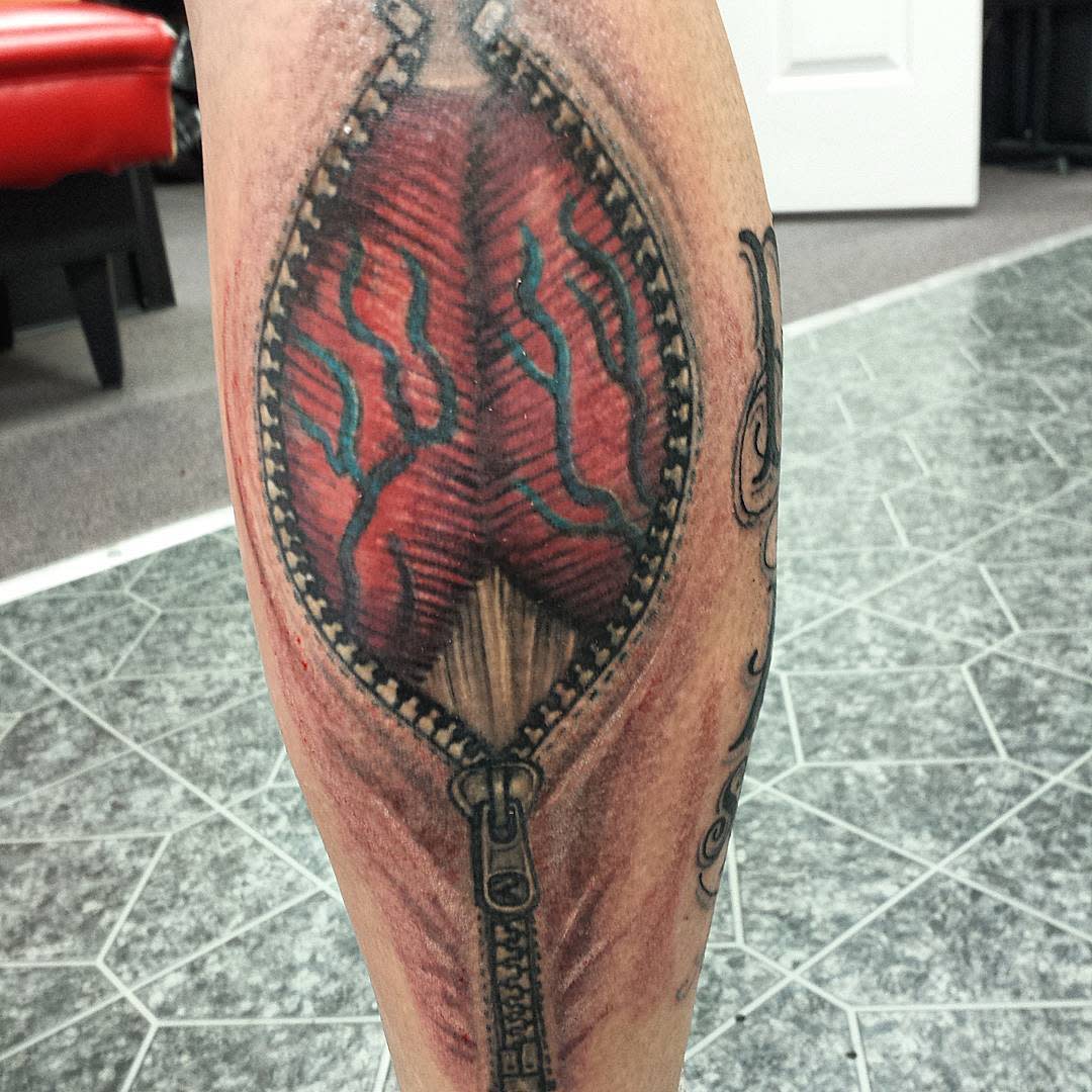 Tattoo of a zipper revealing muscle tissue on the back of a leg