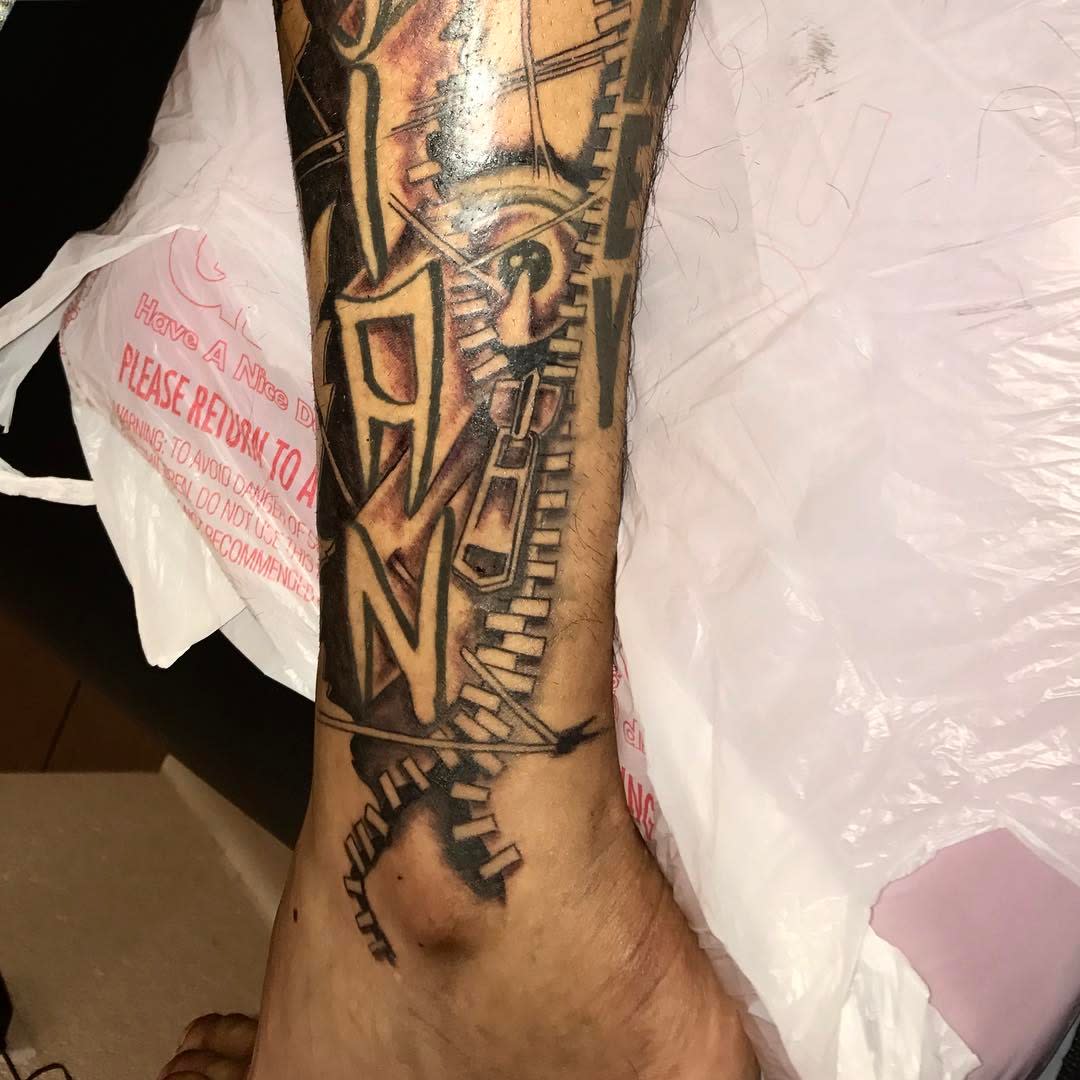 Tattooed leg with artistic design and text against a plastic bag backdrop