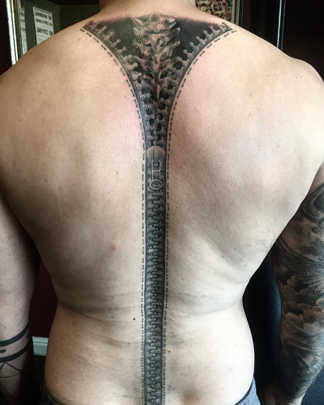Back tattoo featuring an open zipper along the spine with intricate mechanical details
