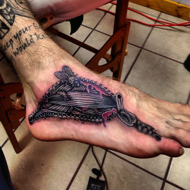 Tattoo of a zipper partially open with a honeybee on the top of a foot