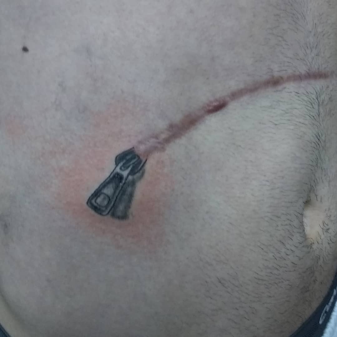 Tattoo of a zipper on skin with a long scar creating the illusion of an unzipped wound