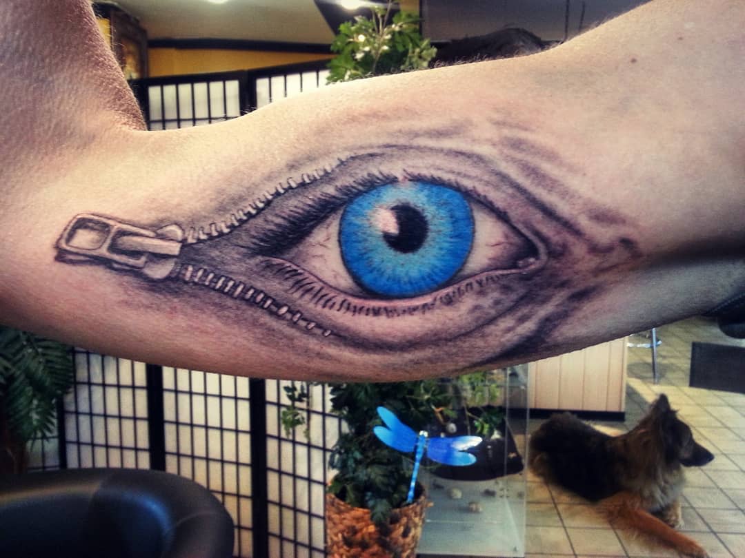 Tattoo of a blue eye with a zipper design on an arm