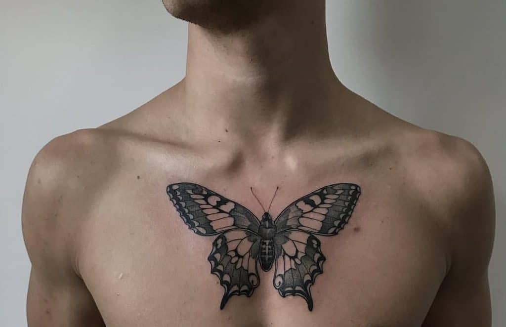 Large black and gray butterfly tattoo on the chest, featuring intricate shading and bold wing details for a striking and symmetrical design.