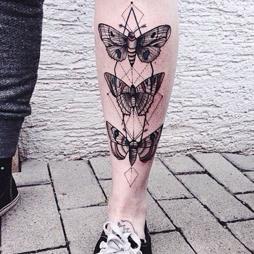 Black and gray tattoo on the lower leg featuring three symmetrical moths with geometric patterns and fine dotwork for a detailed, artistic look.