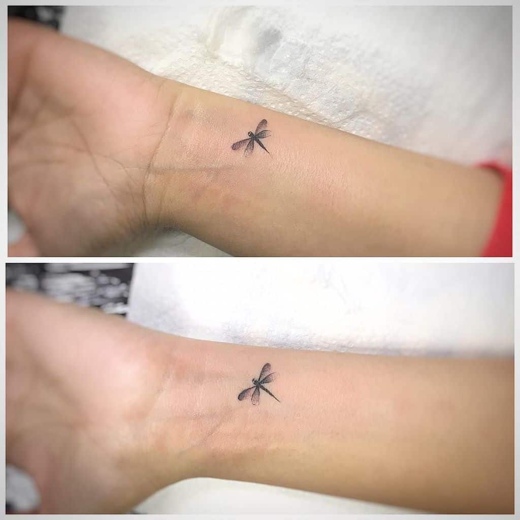 Two tiny dragonfly tattoos on the wrists in fine black ink. The minimal design adds a delicate and subtle touch to the skin.