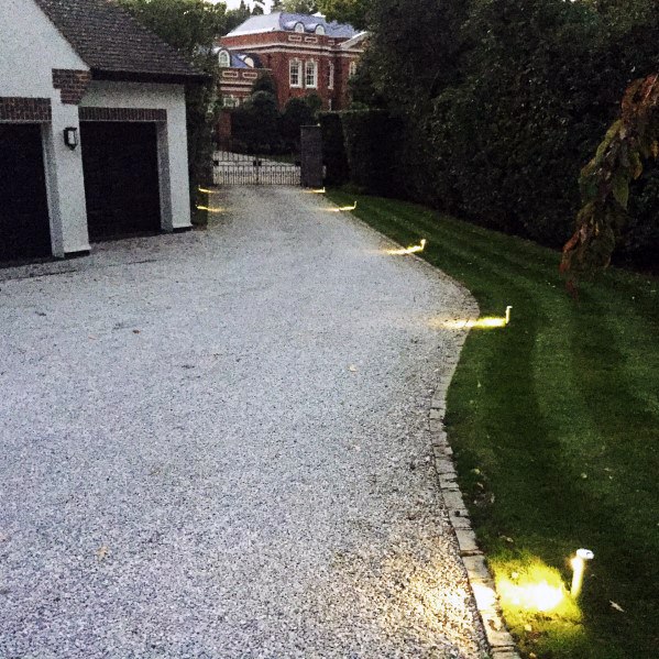 Driveway with low landscape lighting along the edges, illuminating the gravel path and grassy area