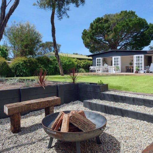 Backyard with a cozy fire pit, wooden bench, and steps leading to a patio surrounded by trees and a house