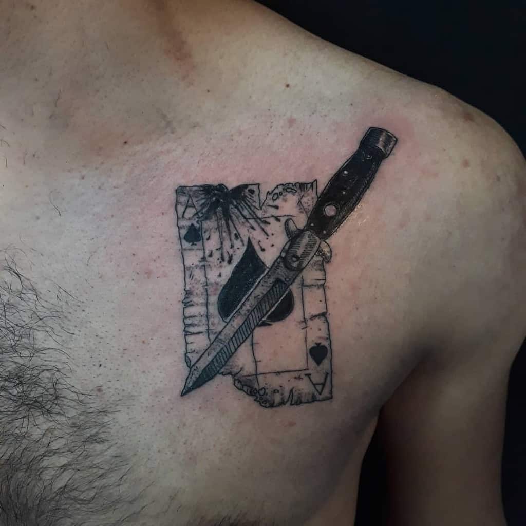 The tattoo depicts a knife piercing through a torn playing card with a ace of spades symbol with splash of blood in the corner