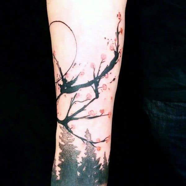 Forearm tattoo featuring an abstract cherry blossom branch with pink flowers, bold black ink strokes, and a forest silhouette below