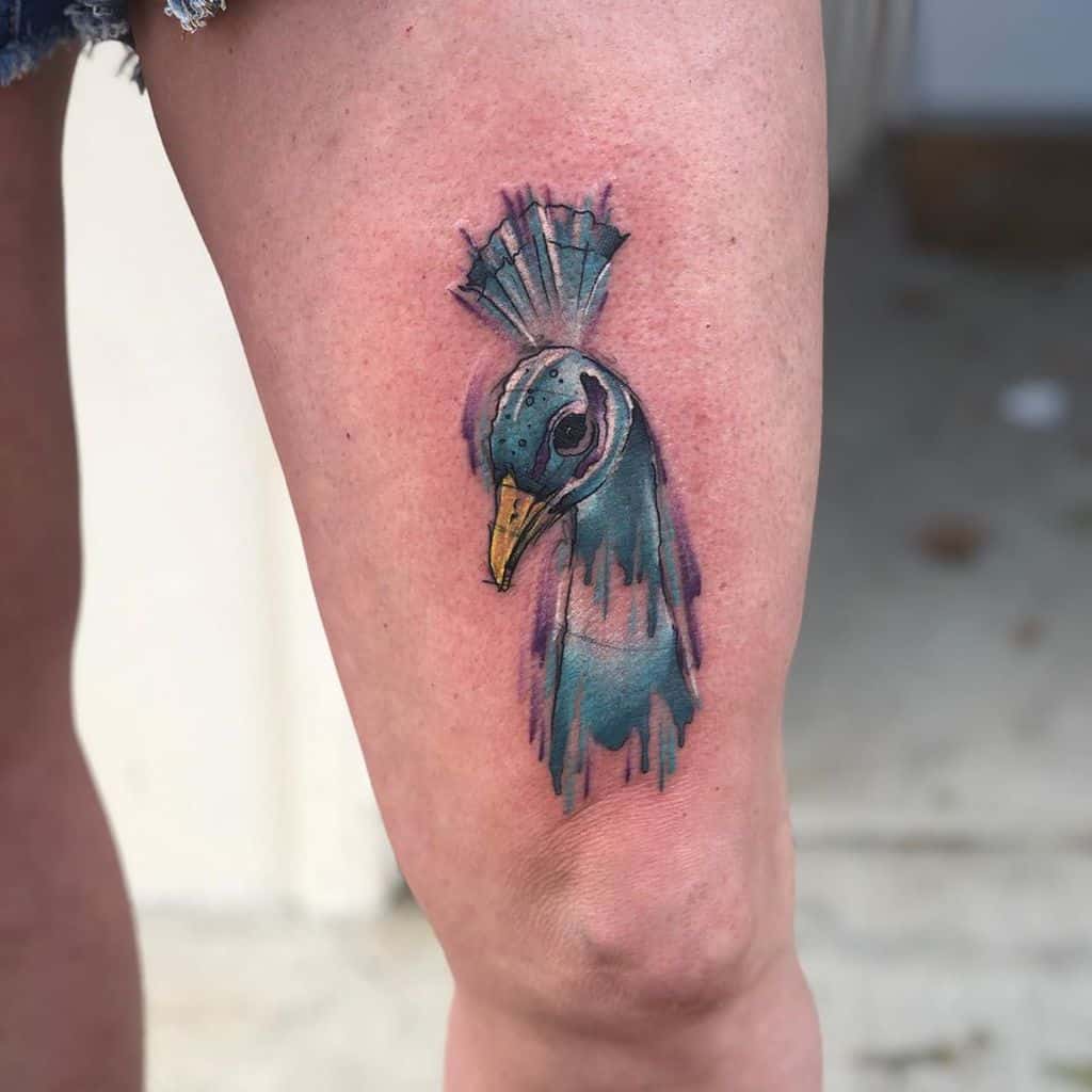 Vibrant peacock tattoo with a watercolor effect on the thigh, featuring teal and blue tones blending into the feathers.