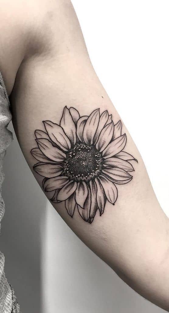 Bold black ink sunflower tattoo on inner arm with intricate shading and fine line details, creating a realistic floral design.