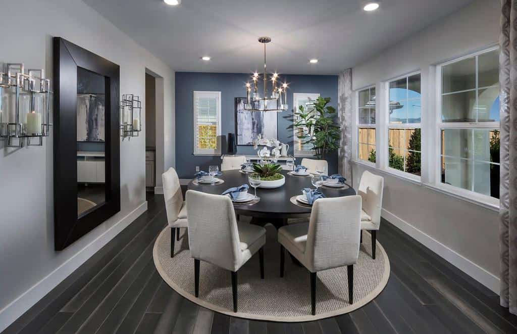 contemporary dining room blue accent wall round black table gray chairs large wall mirror chandelier