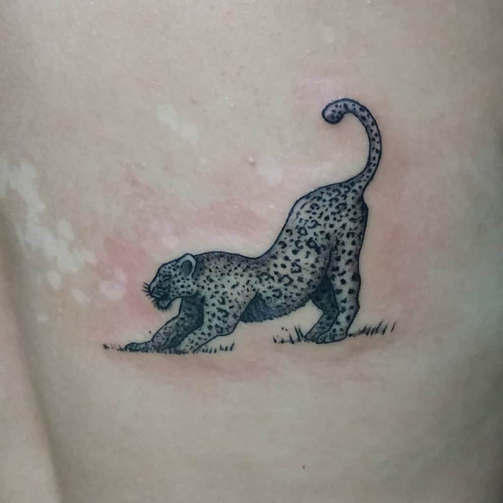 A simple, clean tattoo of a jaguar stretching, with delicate shading and minimalistic detail, placed on the side of the torso.