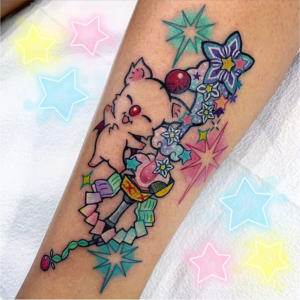 Vibrant Kingdom Hearts tattoo of a cheerful Moogle holding a Keyblade adorned with Wayfinder charms, colorful stars, and magical sparkles.
