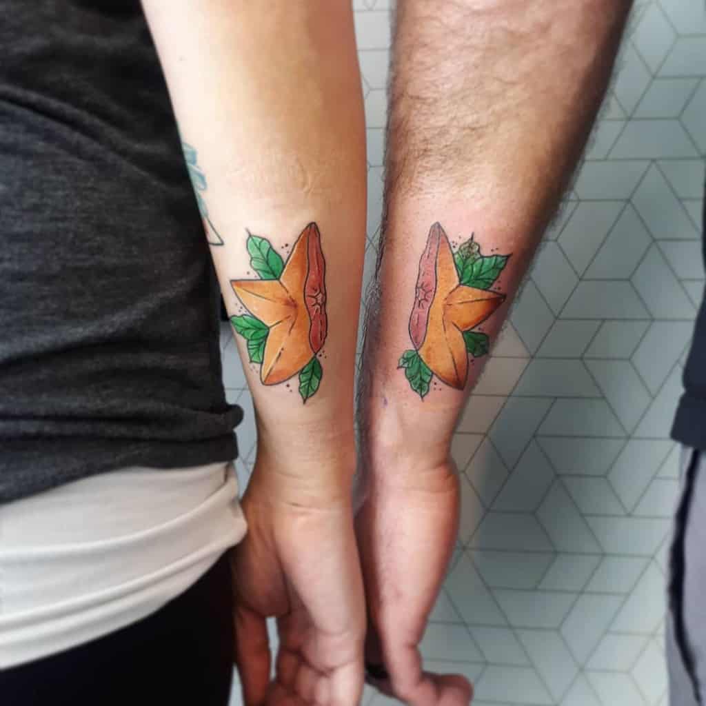 Matching Kingdom Hearts-inspired tattoos of a Paopu fruit, symbolizing eternal connection, inked in vibrant orange and green on forearms.