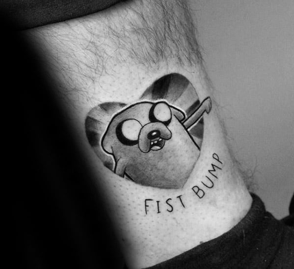 Black and grey tattoo of Jake the Dog from Adventure Time inside a heart shape with the words “Fist Bump” underneath.