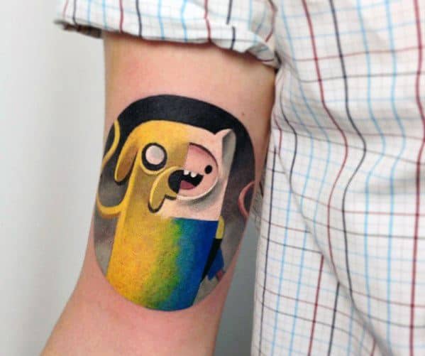 Vibrant Adventure Time tattoo of Finn and Jake in a circular design with bold colors, inked on the back of the upper arm.