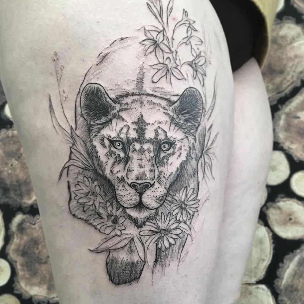 Detailed black and grey lioness thigh tattoo, featuring fine linework, floral accents, and soft shading for a natural and elegant look.