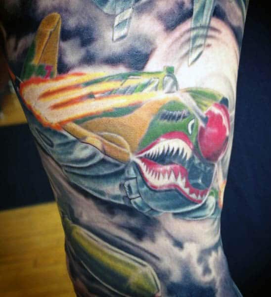 A colorful airplane tattoo with shark teeth flying through a cloudy sky with war-related symbols