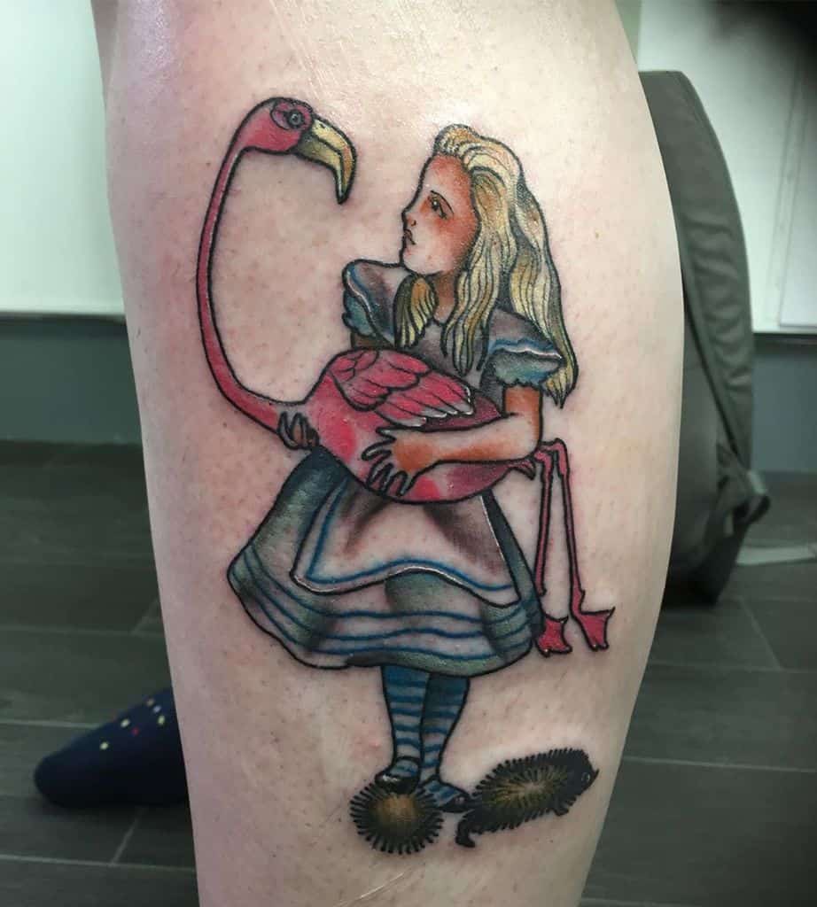 Colorful tattoo of Alice from Alice in Wonderland, holding a flamingo, with a striped outfit and standing on two hedgehogs