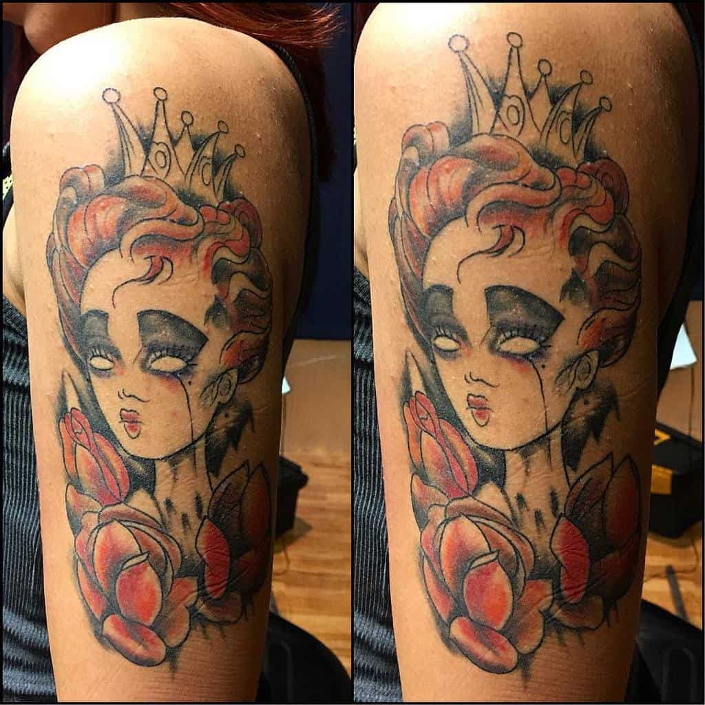 A vibrant upper arm tattoo showcasing the Queen of Hearts from Alice in Wonderland, adorned with striking red roses and a regal crown, blending whimsy with bold artistic flair
