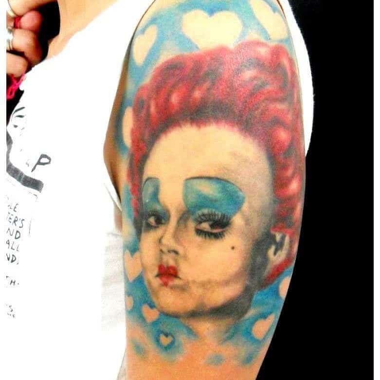 Colorful Queen of Hearts tattoo showcasing bold red hair, dramatic blue eyeshadow, and a background of floating hearts