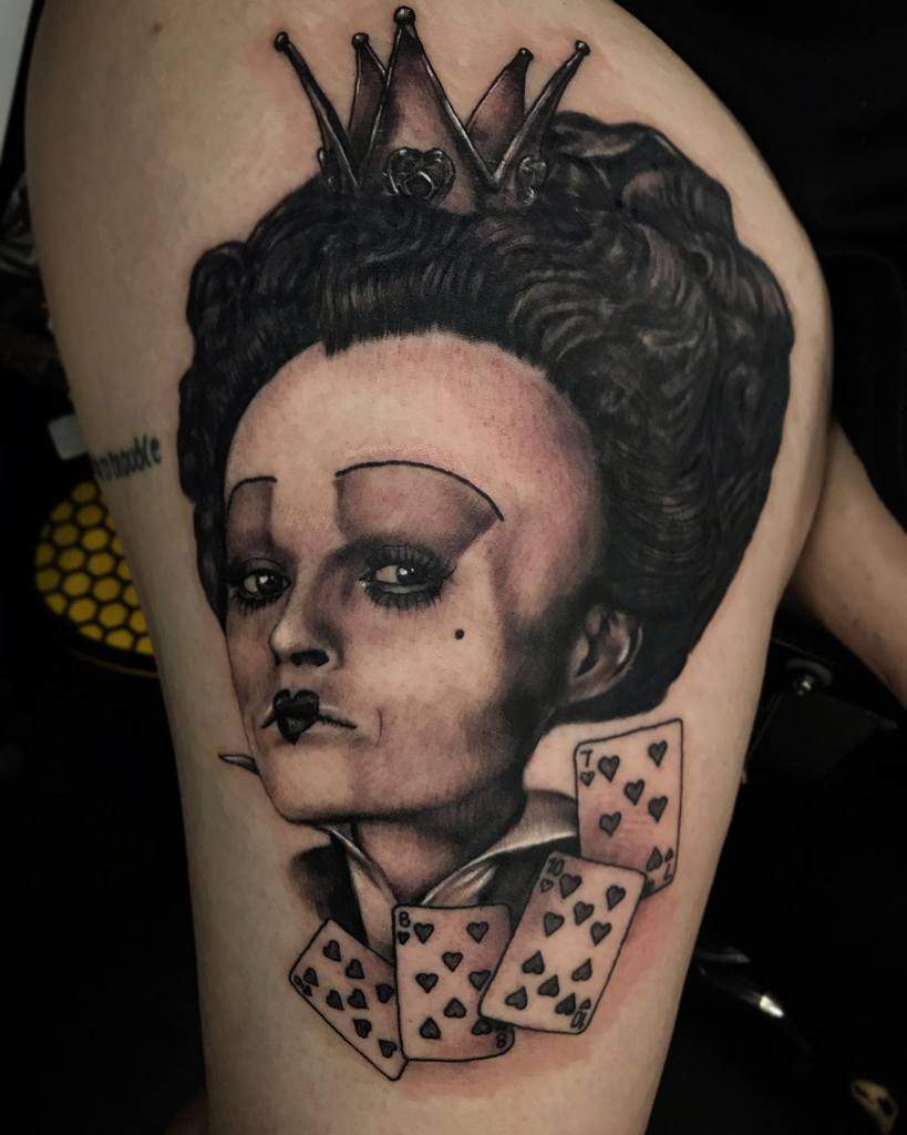 Realistic Queen of Hearts tattoo featuring intricate details, a bold crown, and a cascade of playing cards in grayscale