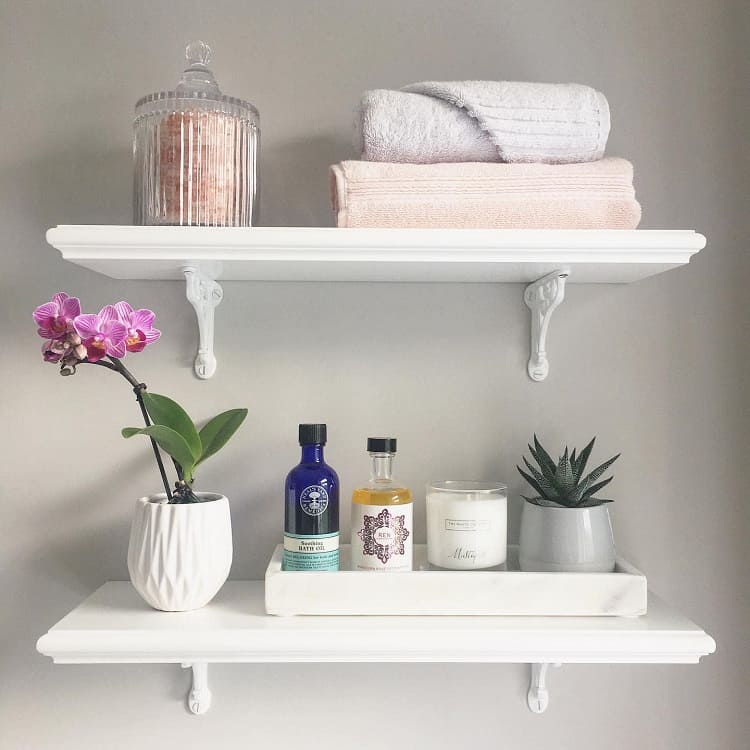 White bathroom shelves with towels, candle, orchid, and skincare products arranged neatly.