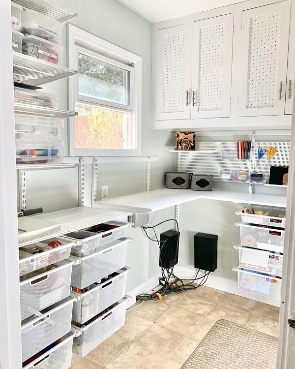 Organized craft room with white shelves, drawers, and a small desk; supplies are neatly stored in clear bins