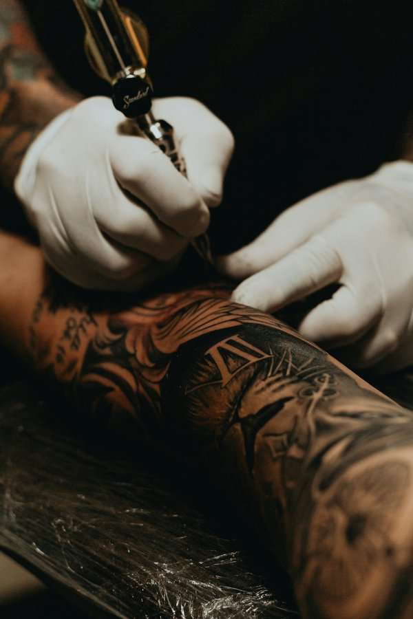White gloved tattooer tattooing an arm sleeve