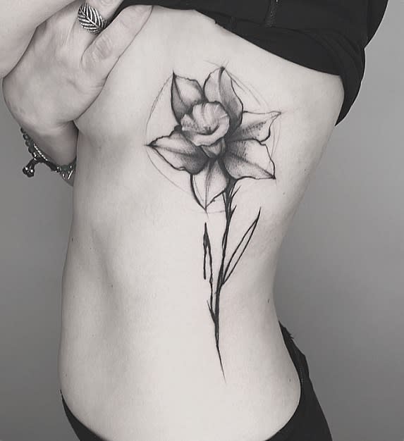 A detailed black-and-white tattoo of a daffodil, with delicate shading that brings out the natural elegance of the flower's structure.