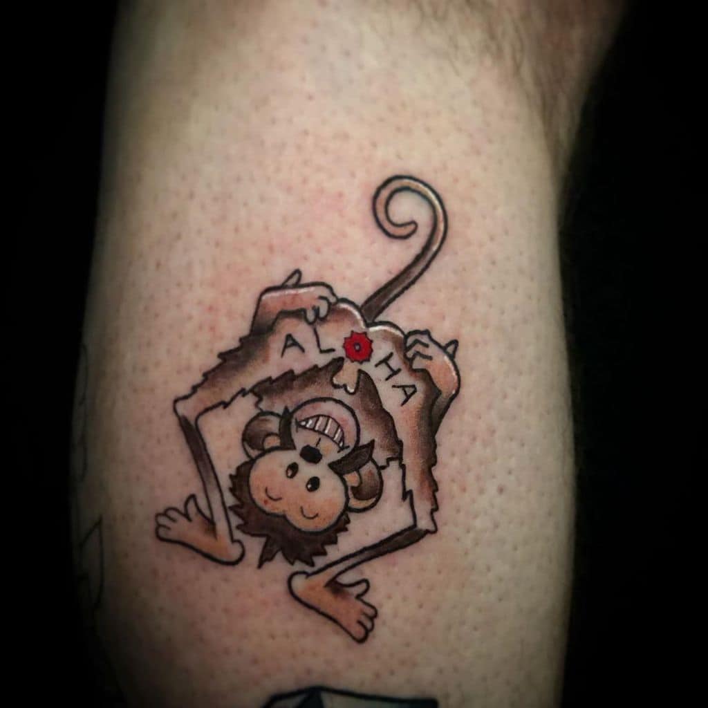 A colorful tattoo of a playful monkey tearing through the skin with 'ALOHA' written on the edges, adding a fun and tropical vibe.