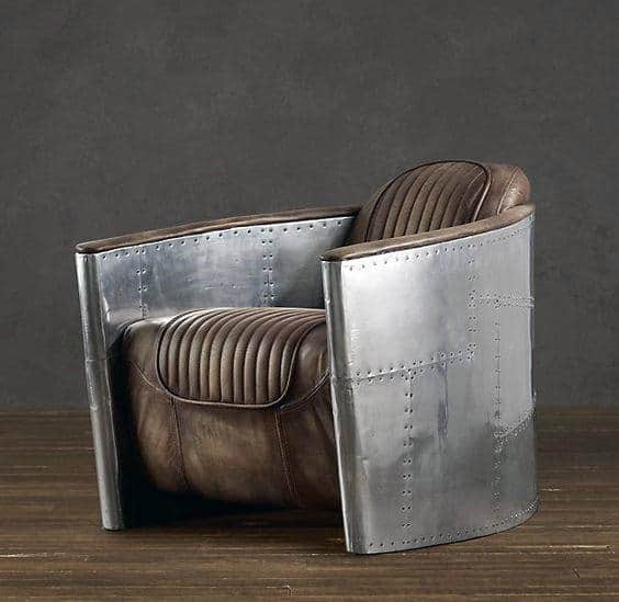 Industrial-style chair with riveted metal sides and brown leather cushions on a wooden floor
