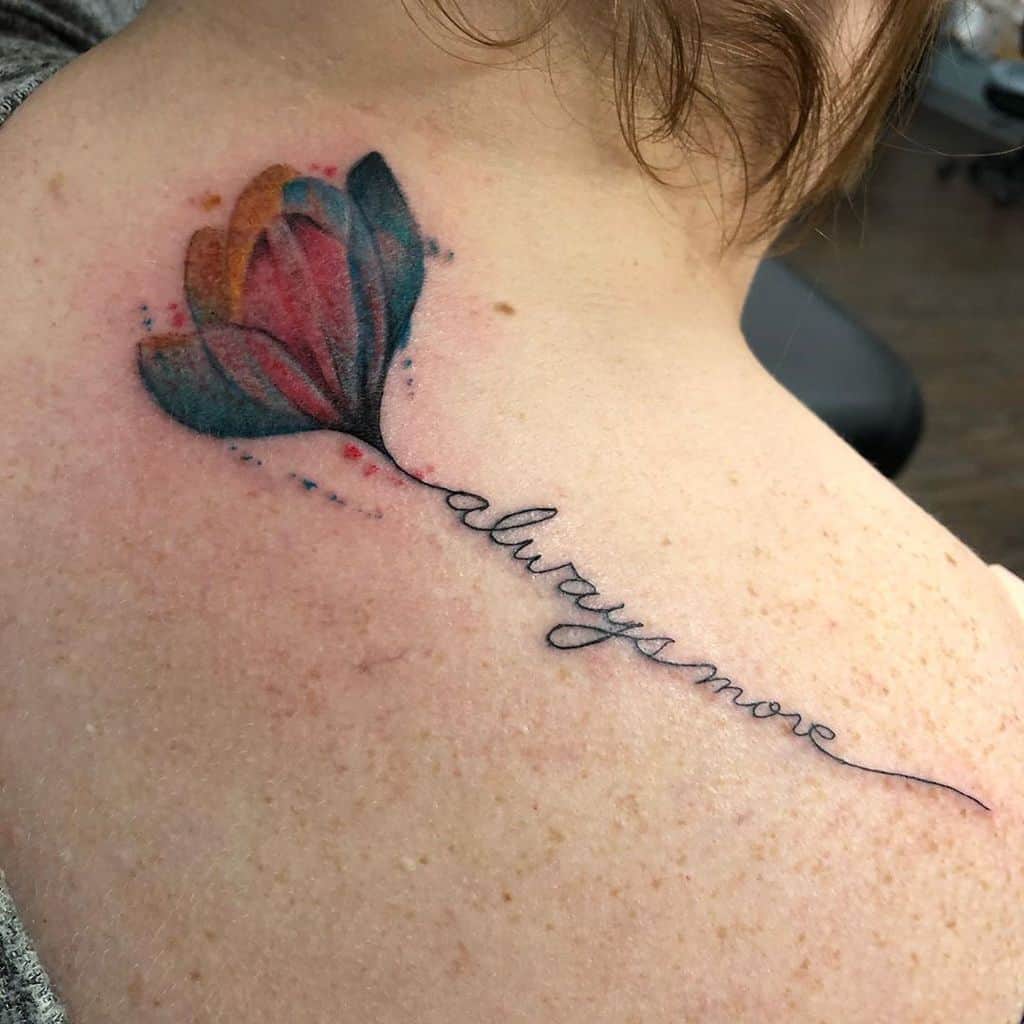 A watercolor tulip tattoo on the upper back, featuring vibrant blue and red petals with a stem that transitions into the cursive phrase "always more."