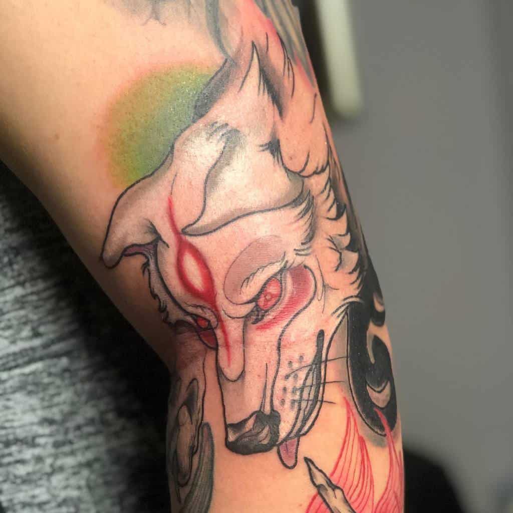 Dynamic Okami tattoo of Amaterasu with intense red markings, bold black accents, and soft shading, creating a fierce and divine expression