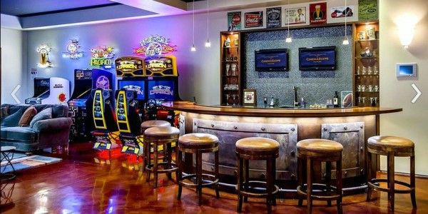 Home bar with arcade games, bar stools, neon signs, and cozy seating area