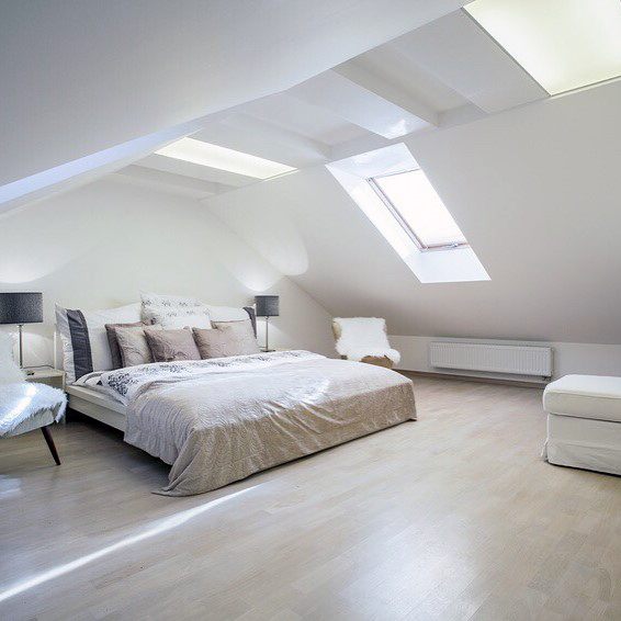 Bright attic bedroom with a sloped ceiling, skylight, cozy double bed, white walls, and minimal decor