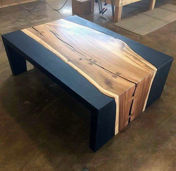Rectangular wood slab coffee table with black accents and natural grain details in a workshop setting.